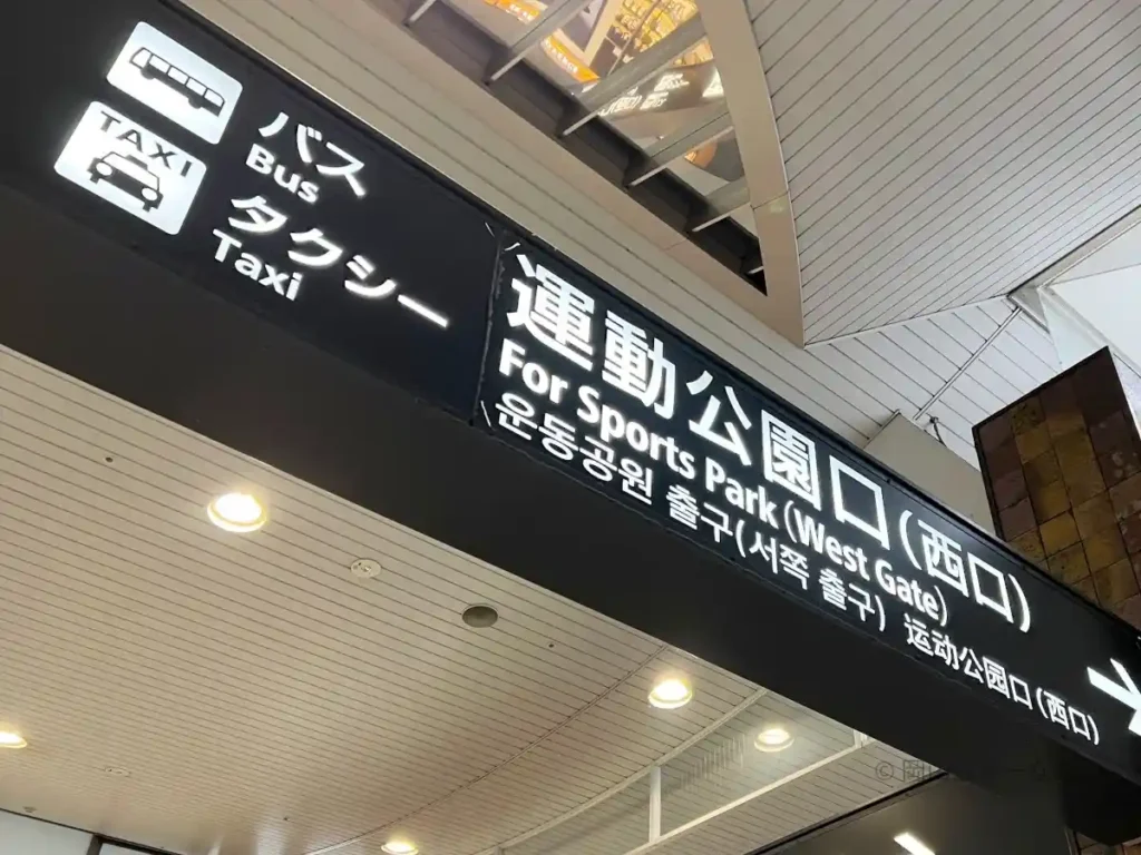 右が運動公園口（西口）への案内板。タクシーの文字が見える。