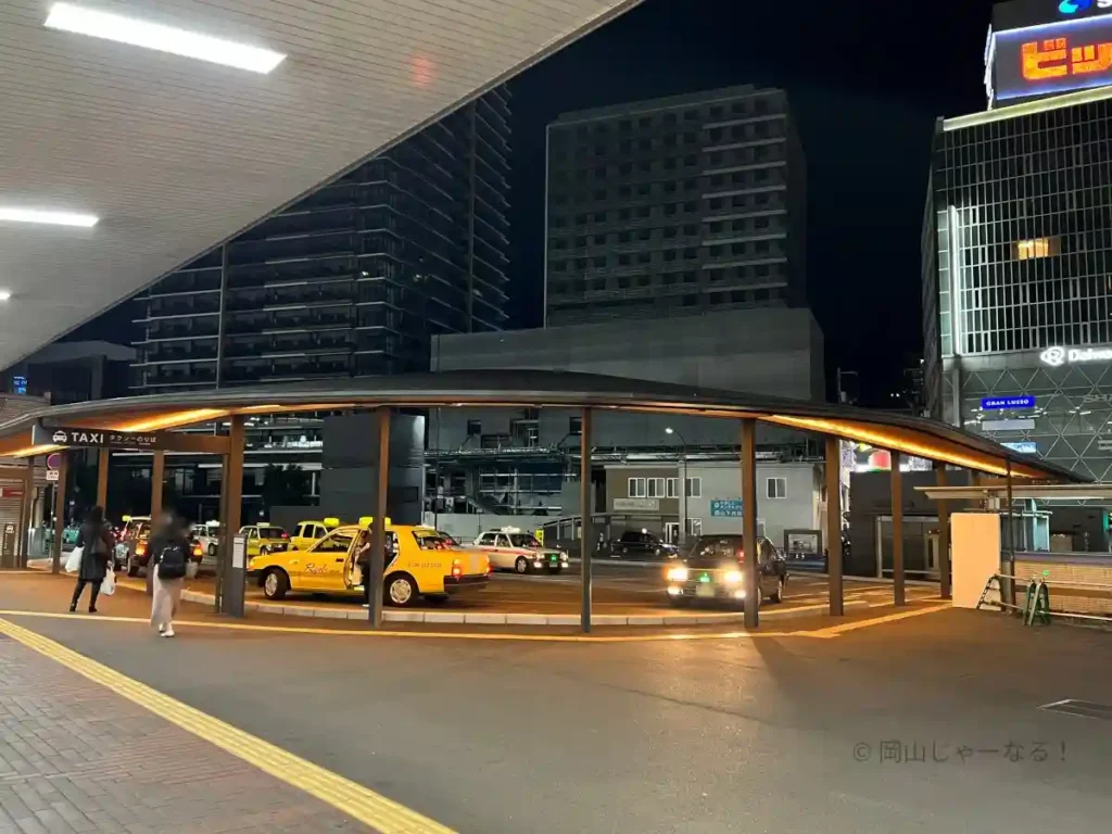 夜21時過ぎの岡山駅東口タクシー乗り場。駅前広場の照明とビルの看板、タクシーのライトで全体が明るく照らされている様子が写っている